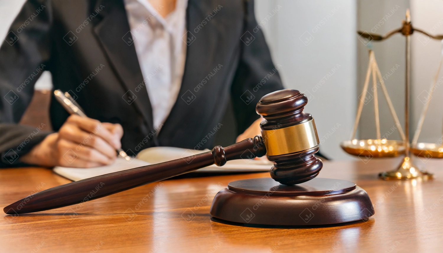 Close-up of gavel on judge desk, symbolizing trial court, justice and legal decisions. A female judge with a pen in her hand takes notes on the background.